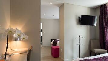 Une chambre d’hôtel comprenant un lit, un bureau avec une chaise, un téléviseur fixé au mur et un petit pouf rose.