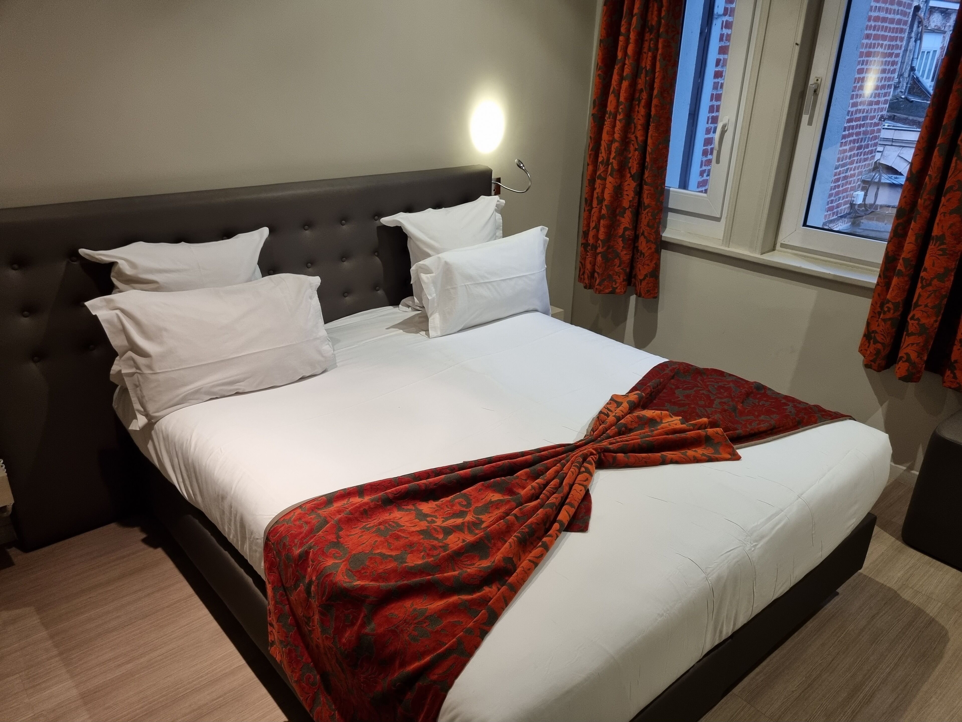 Una cama bien hecha con sábanas blancas y una manta roja estampada.