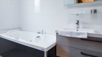 A modern bathroom with a large bathtub, a separate sink, and a vanity with drawers.