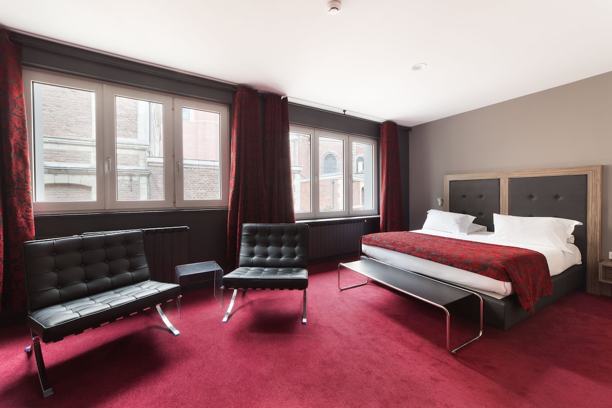 A hotel room with a bed, two chairs, a window, and a radiator.