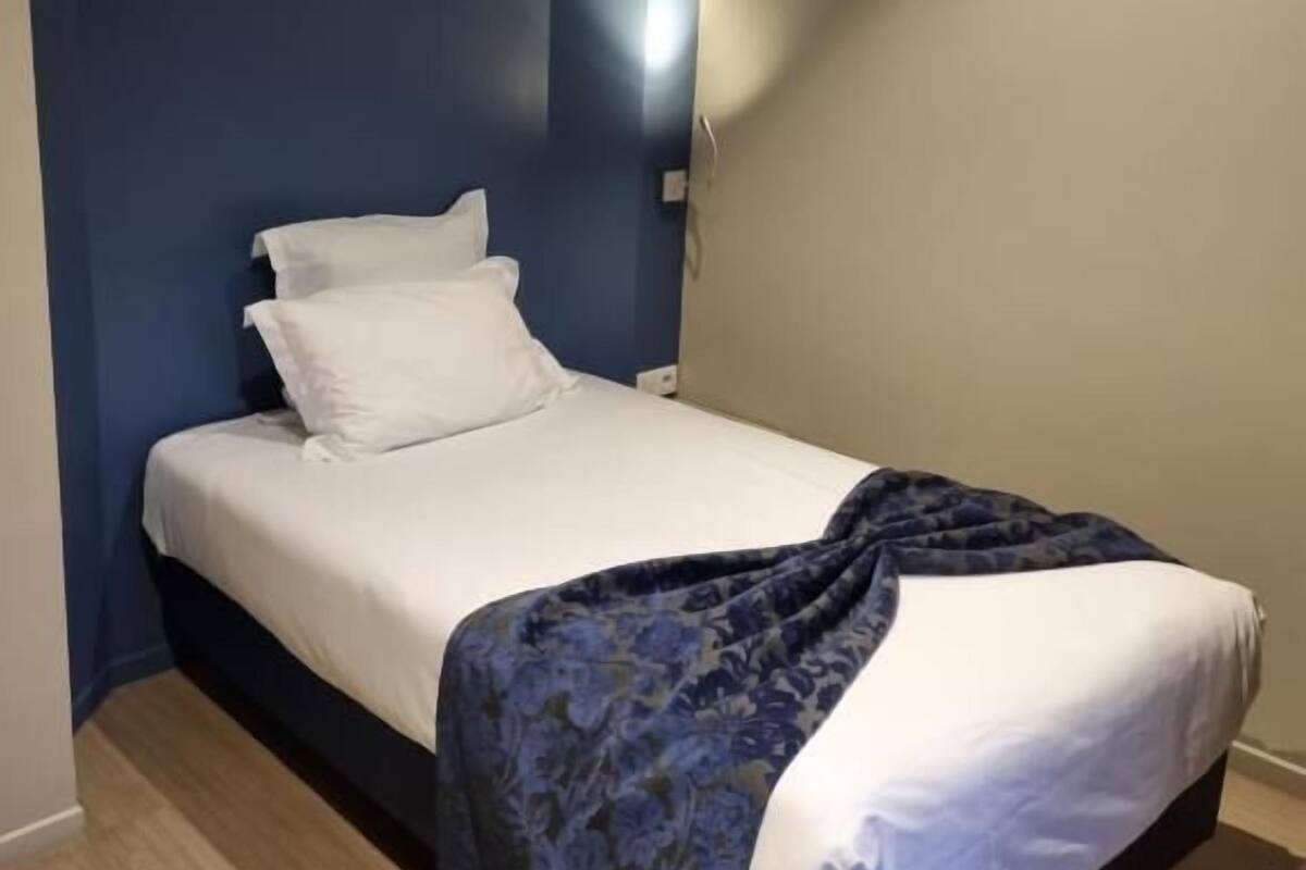 A single bed with white linens and a dark blue floral throw blanket.
