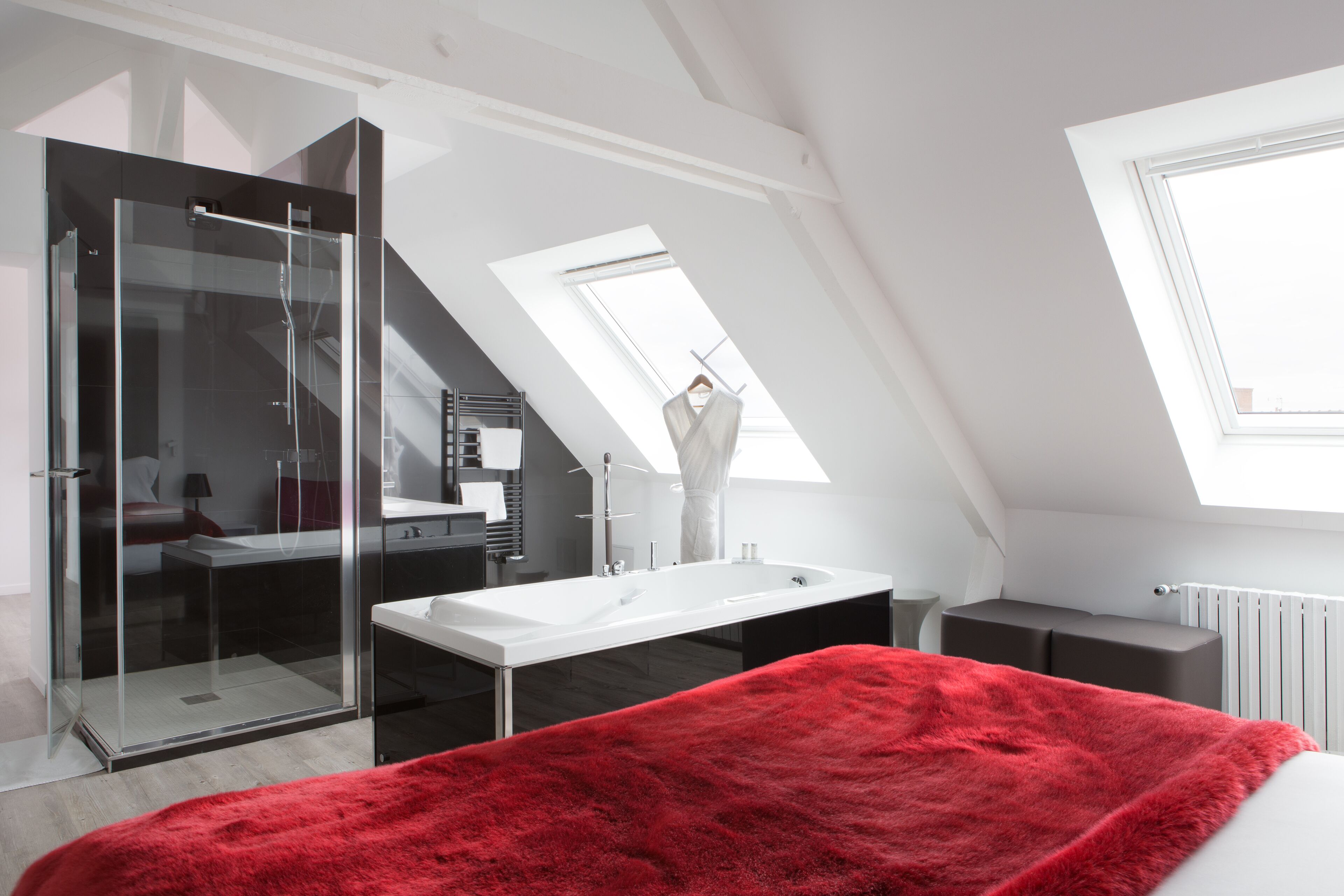 Une chambre moderne avec une douche en verre, une grande fenêtre et une couverture rouge sur le lit.