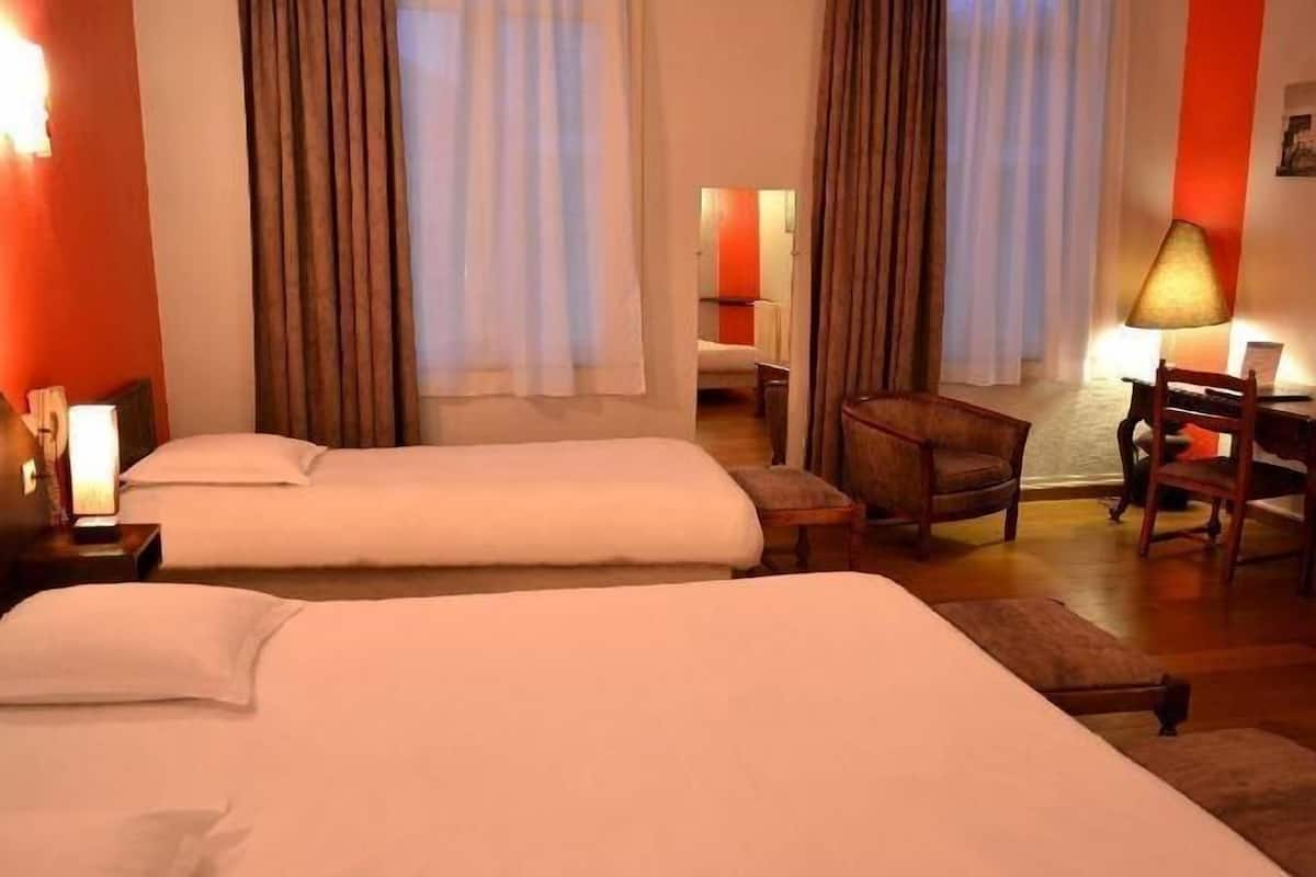 Habitación de hotel con dos camas, un escritorio, una silla y una lámpara.