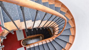 Una escalera de caracol con barandillas de madera y un rellano cubierto de alfombra roja.