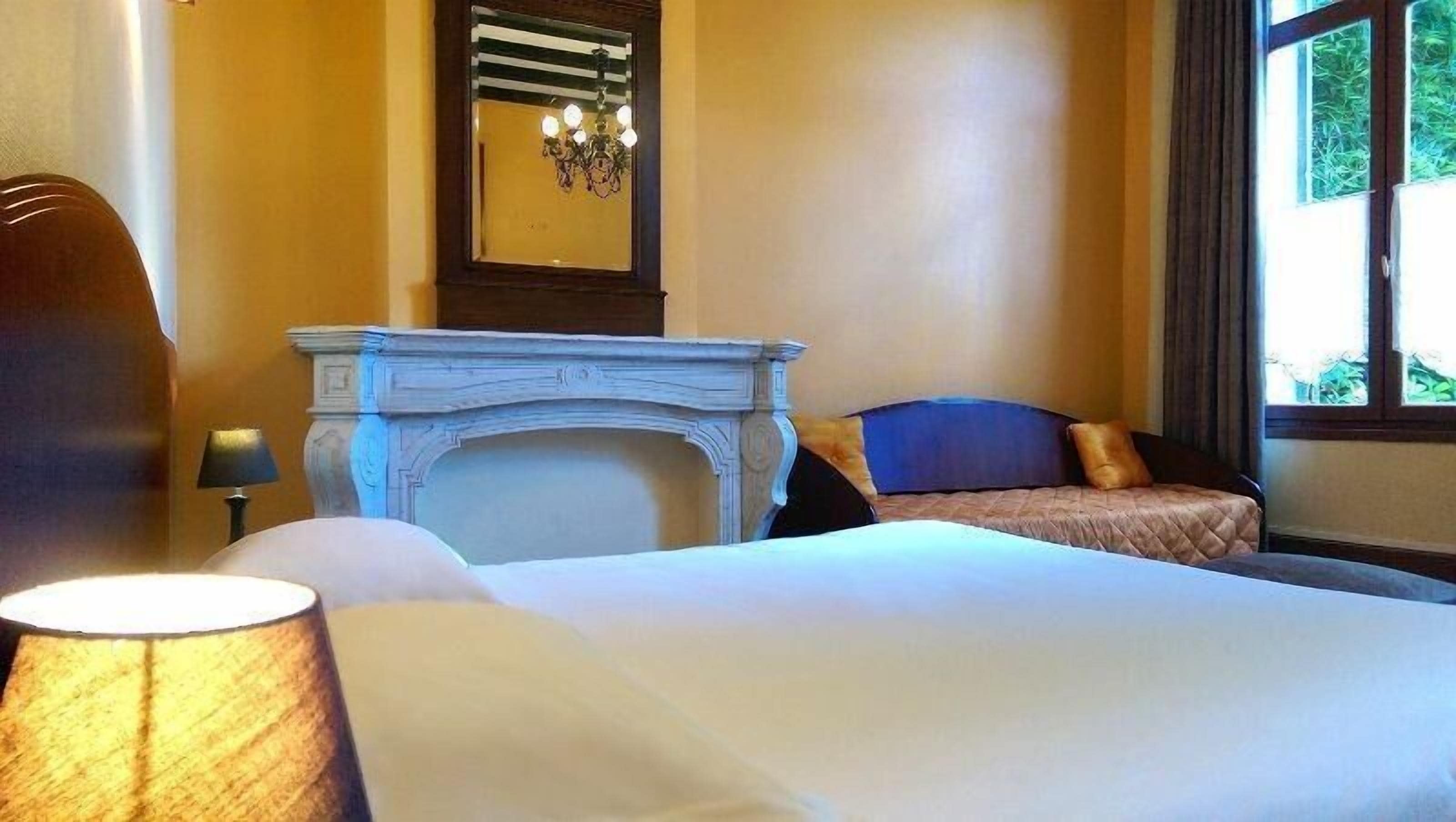 Una camera d'albergo con un letto, un caminetto, una finestra e una lampada.