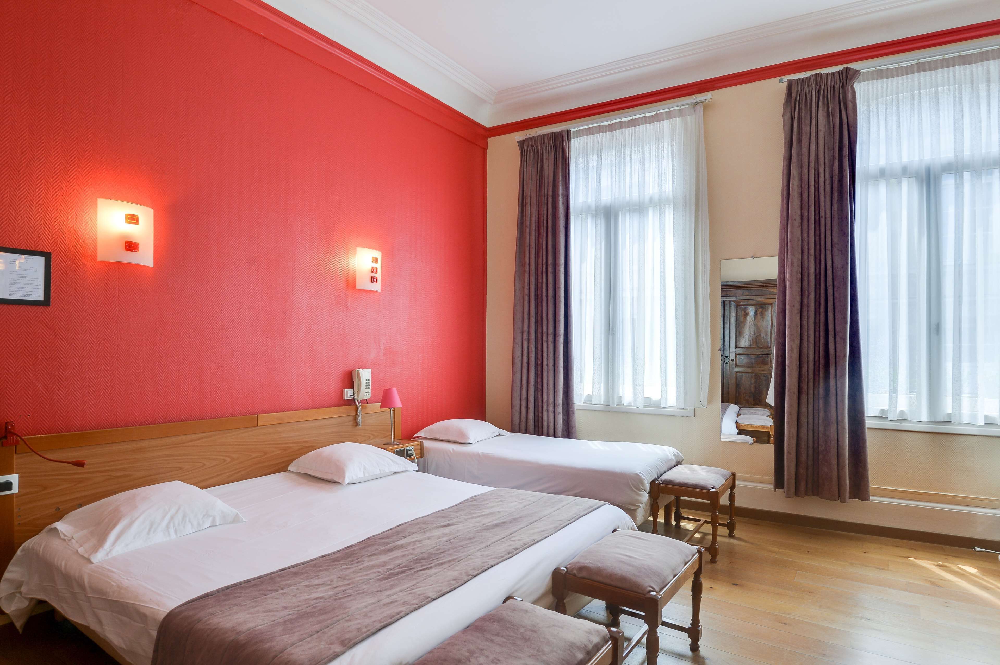 Habitación de hotel con dos camas, cabecero de madera, espejo y ventana con cortinas.