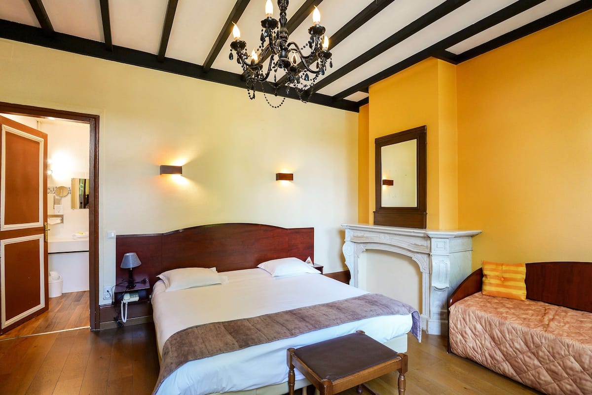 Una habitación de hotel con una cama grande, una mesita de noche, una lámpara, una chimenea y un espejo en la pared.