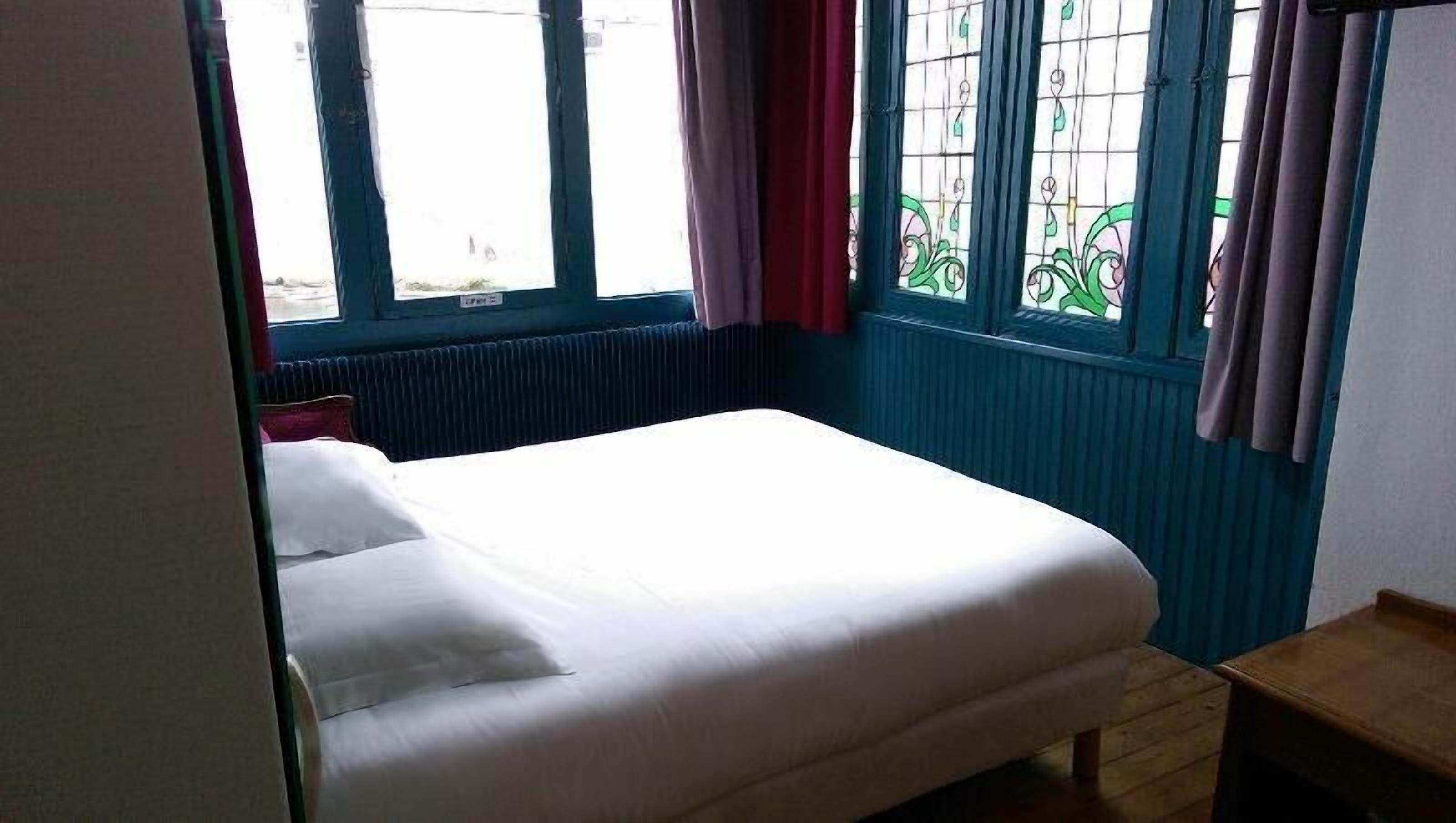 A small, single-bed room with a window, a radiator, and a wooden nightstand.
