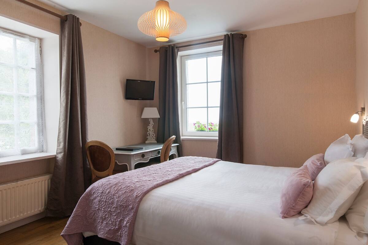 A bedroom with a bed, a desk, a chair, a television, and a window with curtains.