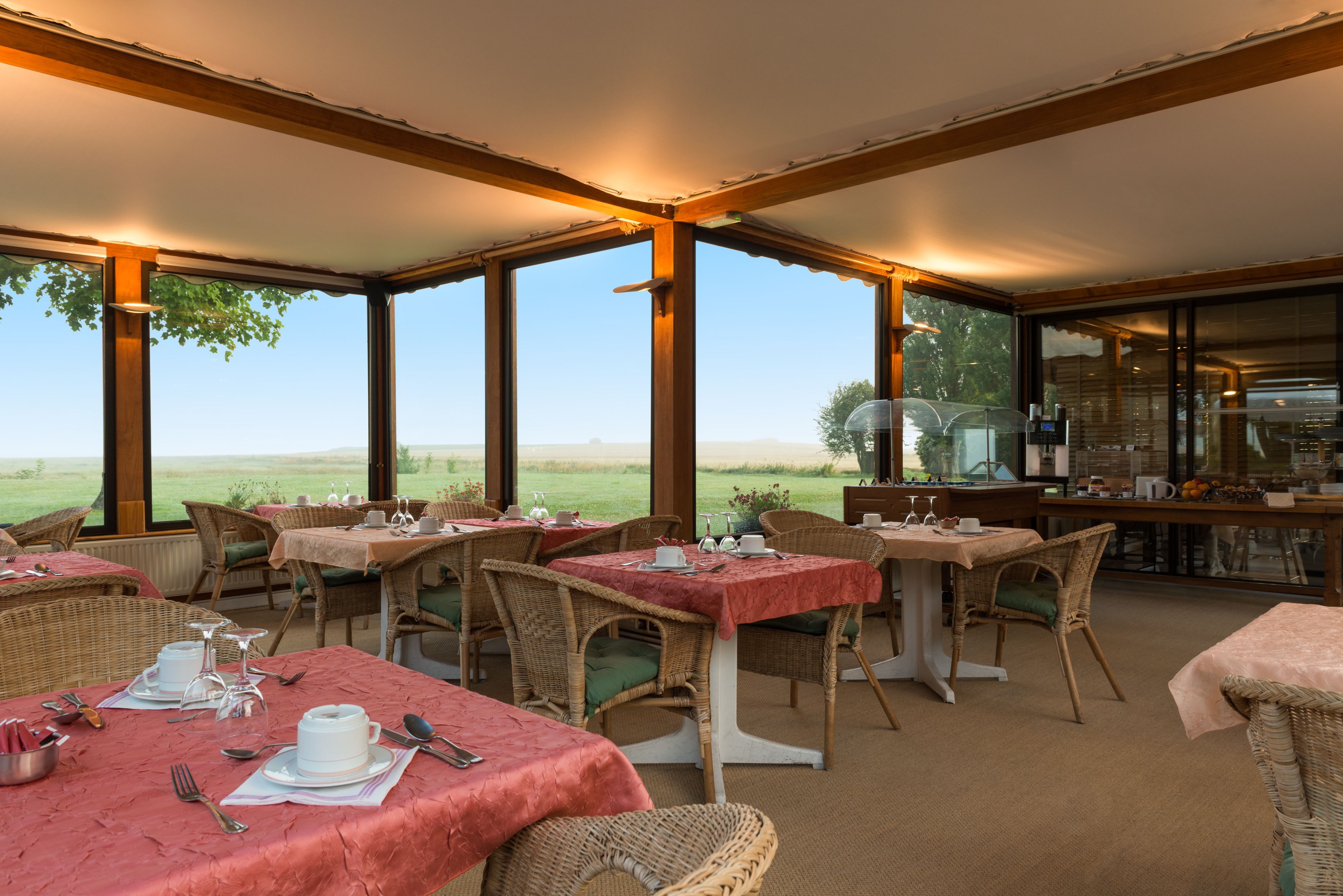 Un restaurante con mesas dispuestas para comer, sillas de mimbre y vistas al exterior.