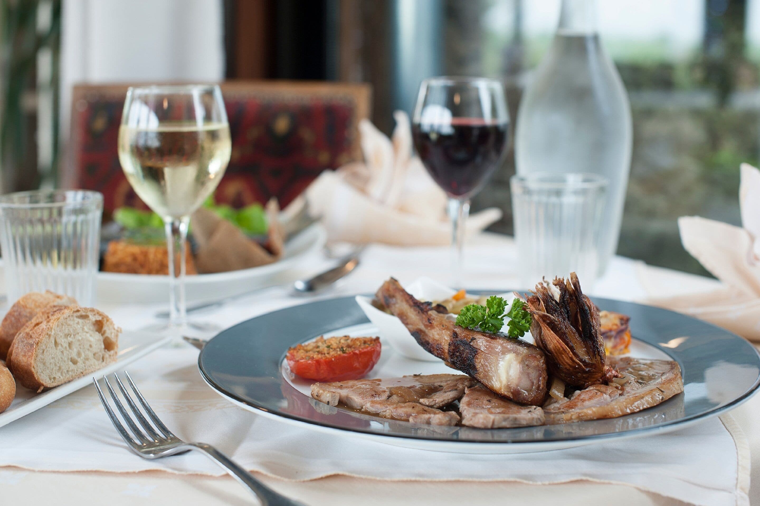 Une table à manger avec des assiettes remplies de nourriture, des verres de vin et une fourchette.