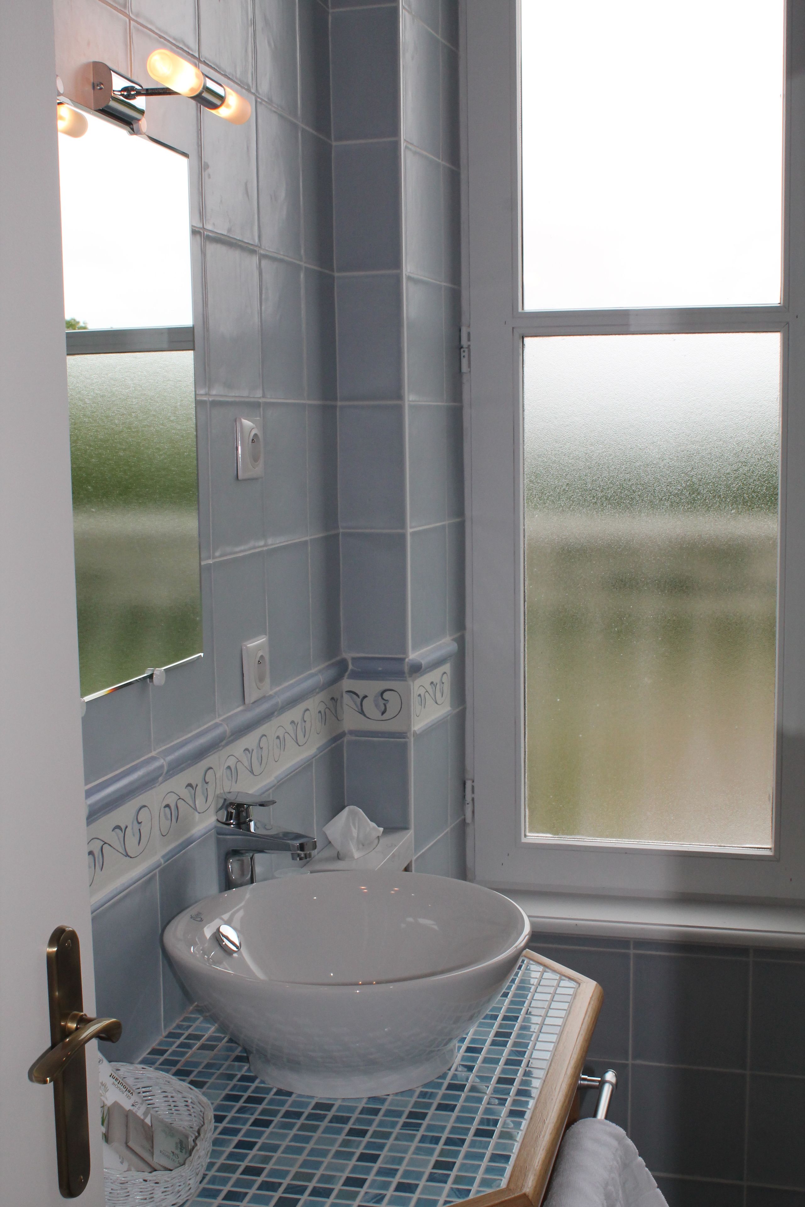 Une salle de bain avec un lavabo blanc, un miroir et une fenêtre.