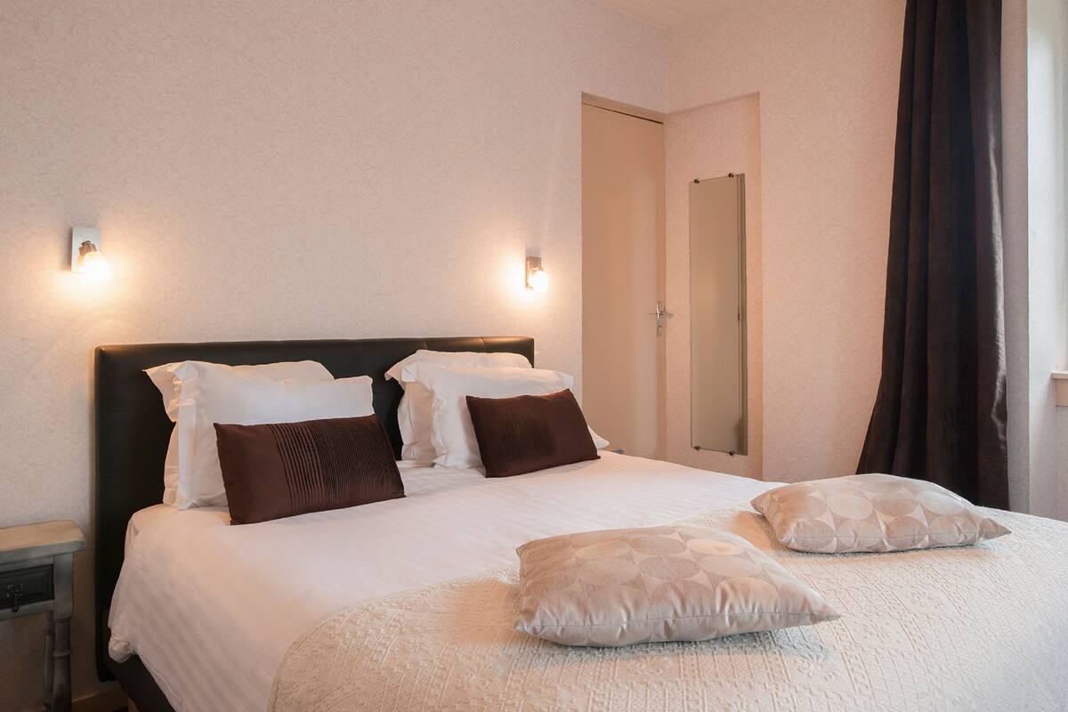 A neatly made bed with white and brown bedding, a dark headboard, and two wall-mounted lights.
