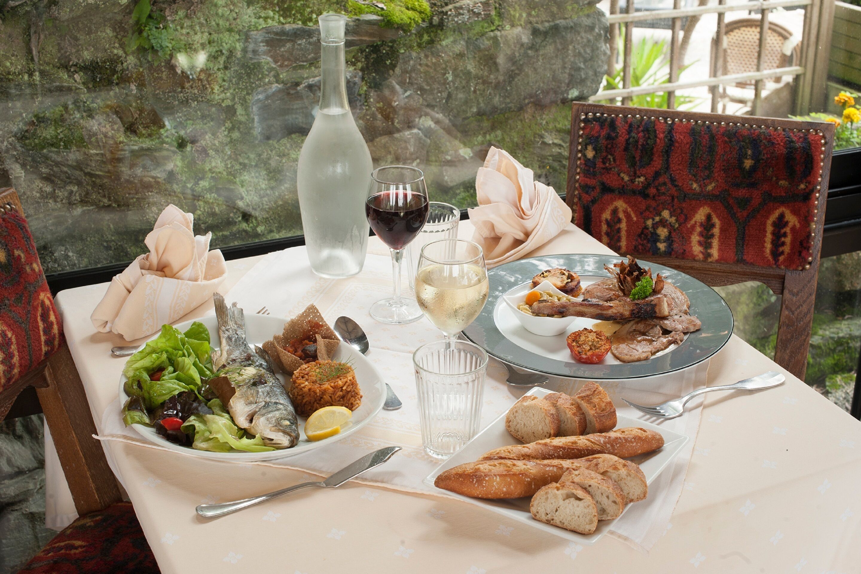 A dining table with a variety of dishes, including fish, bread, and a salad, along with wine glasses and a bottle.