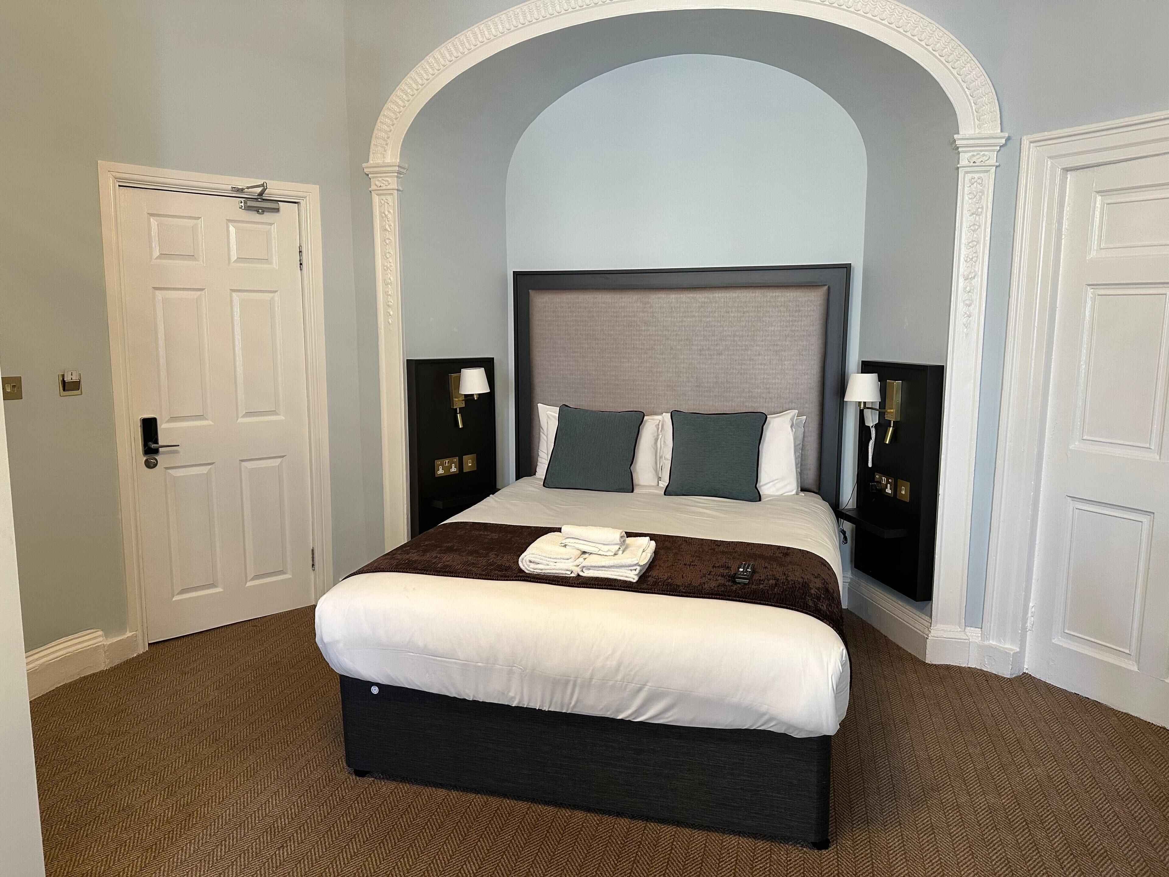 A hotel room with a large bed, two bedside tables, a headboard, and an arched doorway.