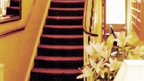 A staircase with a handrail and a chandelier above. - Arran House Hotel (London)