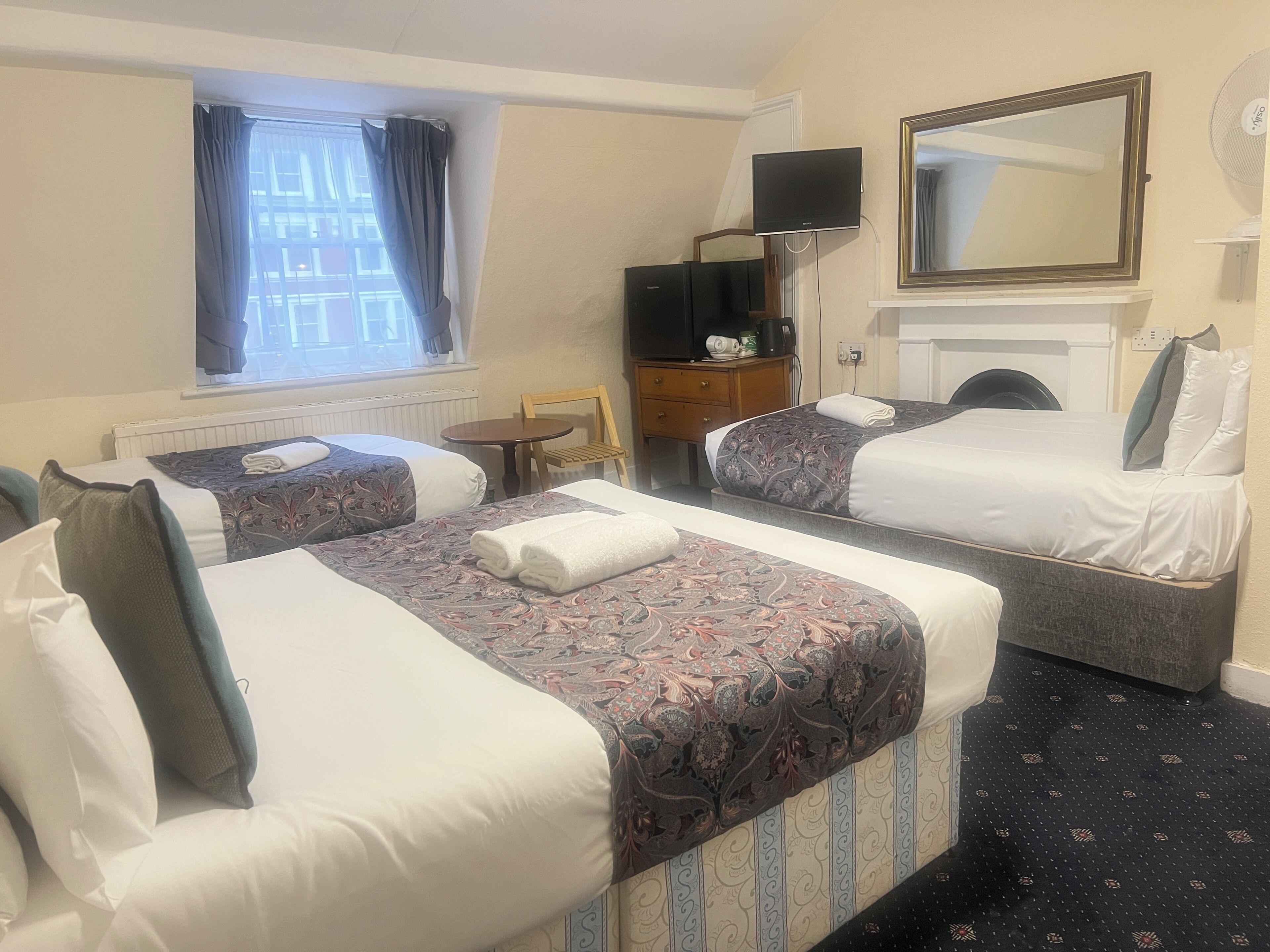 A hotel room with two beds, a desk, a chair, a television, a mirror, and a window with curtains.