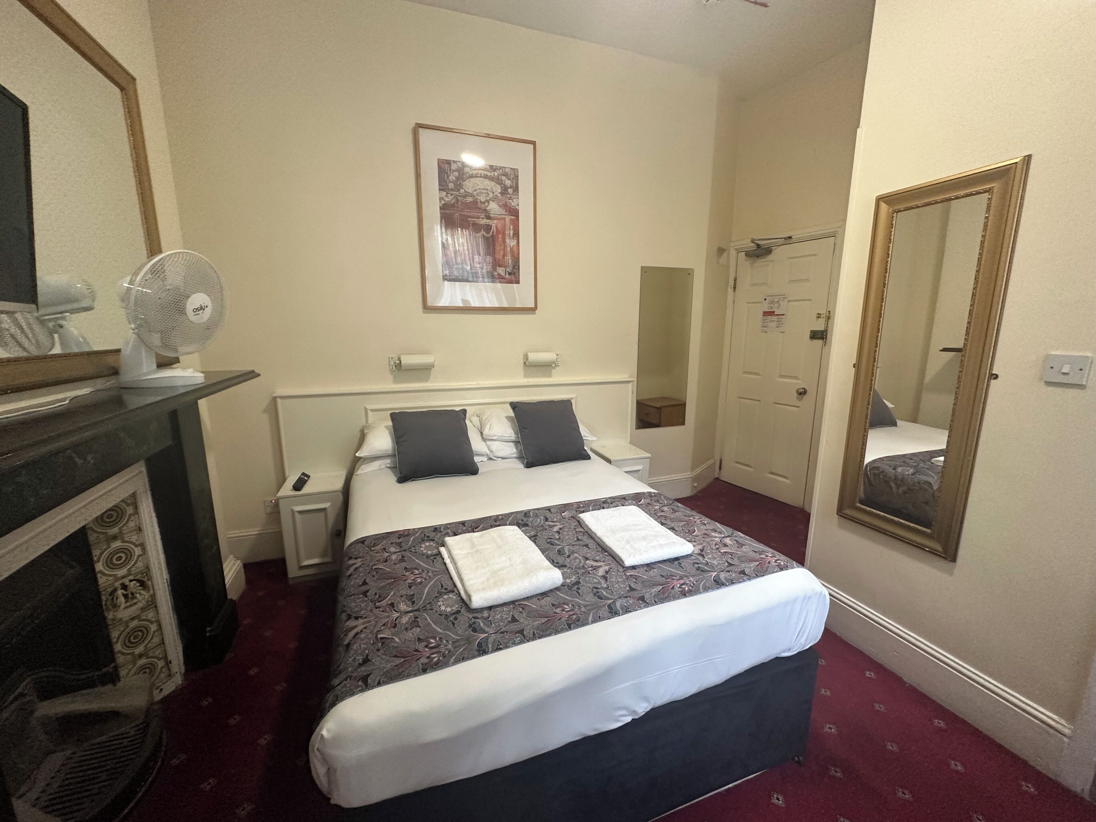 A hotel room with a bed, a mirror, a fireplace, and a framed picture on the wall.