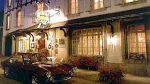 A traditional building with a signboard, a parked car, and potted plants. - Hôtel Eychenne (Saint-Girons)