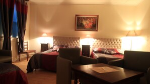A hotel room with two beds, a wooden floor, a tufted headboard, two bedside tables with lamps, a wooden coffee table, and a painting on the wall. - Hôtel Eychenne (Saint-Girons)