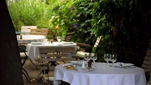 An outdoor dining area with tables set for two, covered with white tablecloths, surrounded by greenery and plants. - Hôtel Eychenne (Saint-Girons)