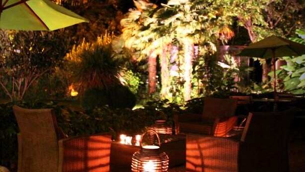 An outdoor seating area with wicker furniture and lanterns, surrounded by lush foliage and trees. - Hôtel Eychenne (Saint-Girons)