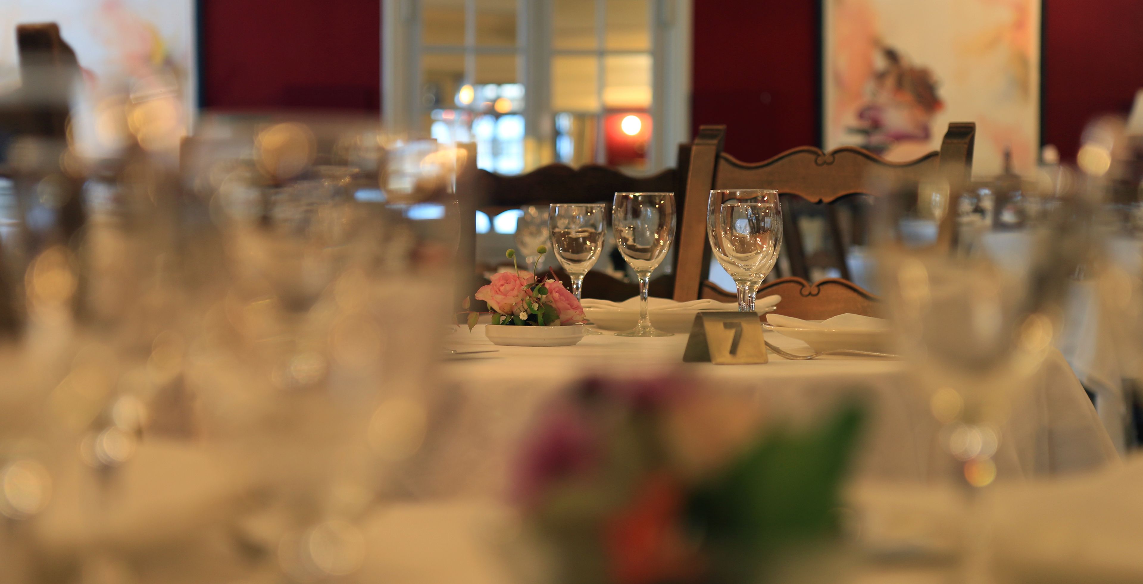 A dining table set with wine glasses, a number card, and a flower arrangement.