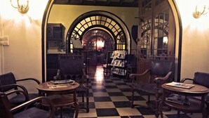 A checkered floor, wooden chairs, and tables in a hallway with arched ceilings and wall-mounted lights. - Hôtel Eychenne (Saint-Girons)