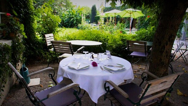 An outdoor dining area with round tables set for four, surrounded by wooden benches and chairs. - Hôtel Eychenne (Saint-Girons)