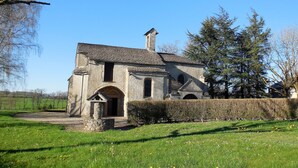 Un bâtiment en pierre doté d’une cheminée, de fenêtres en arc de cercle et d’une petite entrée.