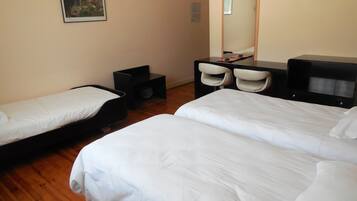A hotel room with two single beds, a desk with a chair, a TV, and a small table.