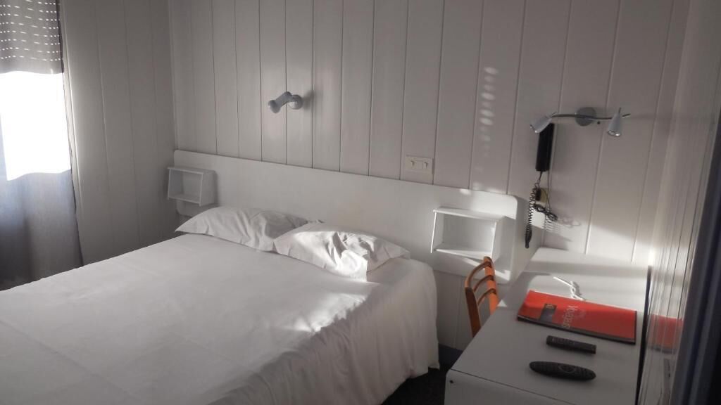 A hotel room with a bed, bedside table, nightstand, and a mirror.