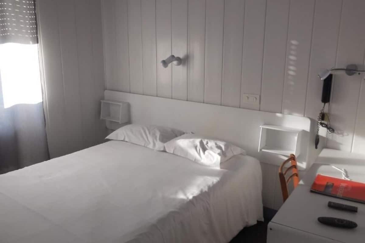 A hotel room with a bed, bedside table, nightstand, and a mirror.
