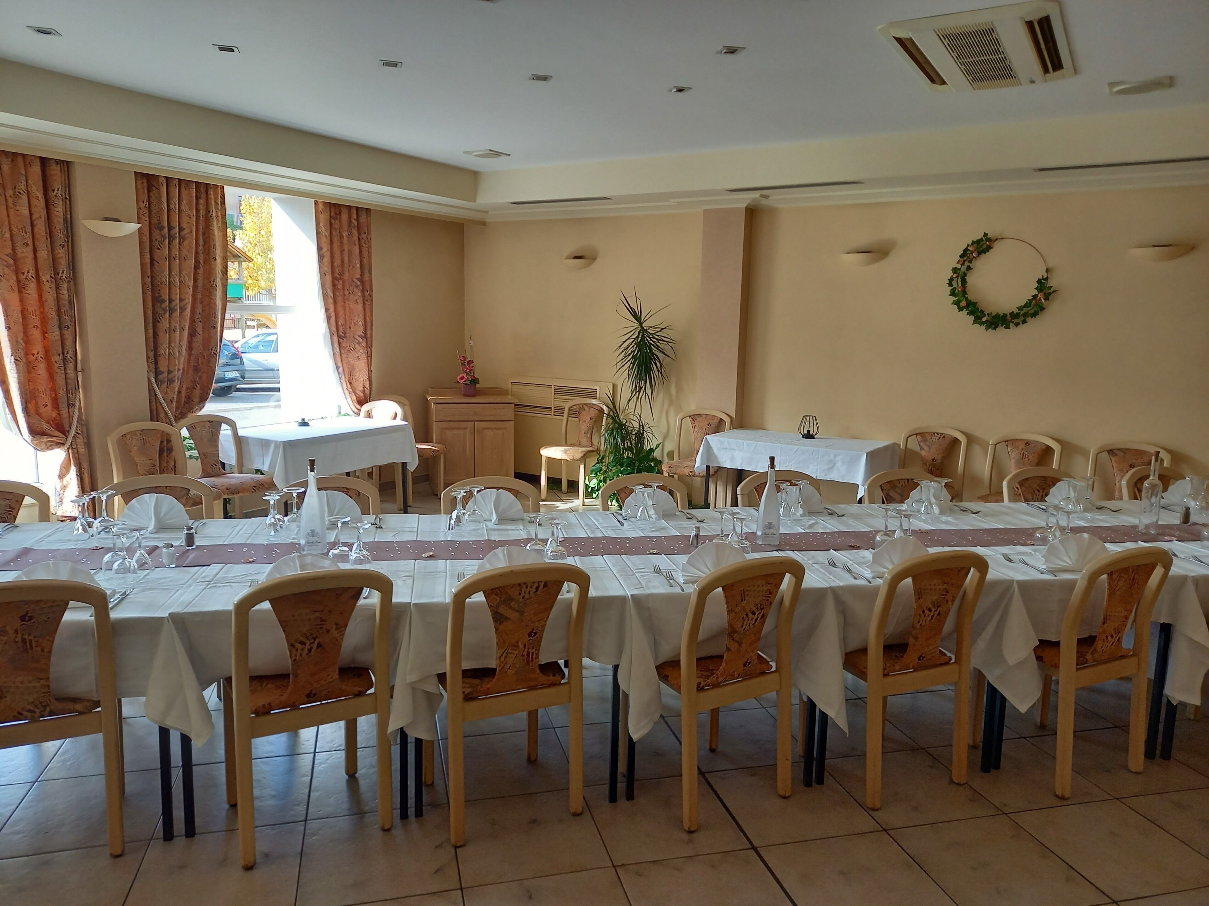 Un espace repas avec plusieurs tables dressées pour le repas, agrémenté de nappes blanches et de chaises en bois.