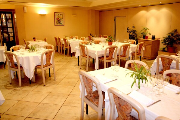 Comedor con varias mesas dispuestas para comensales, sillas y plantas en macetas.