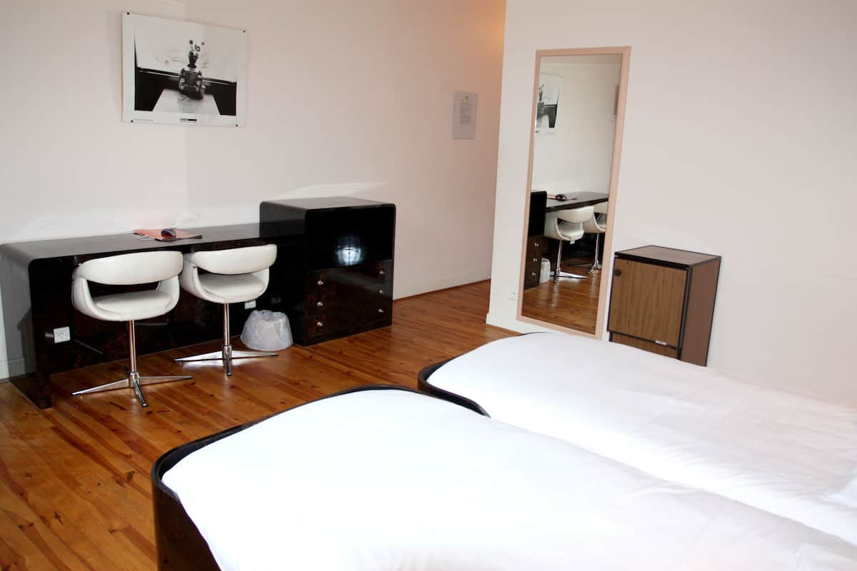 Een hotelkamer met een houten vloer, een bed, een bureau met twee stoelen, een spiegel en een klein kastje.