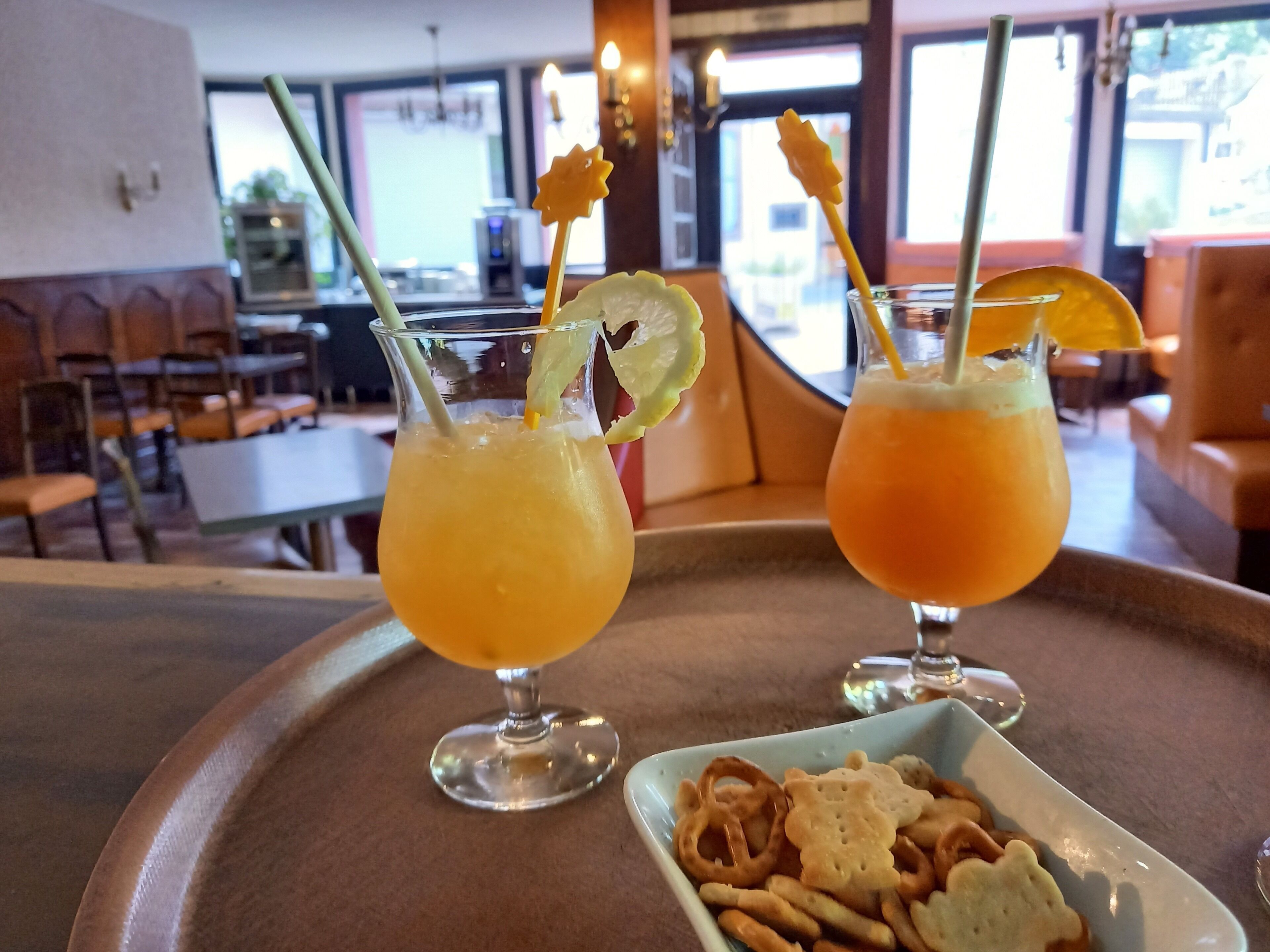 Duas bebidas com guarnições de frutas sobre uma bandeja em um restaurante.