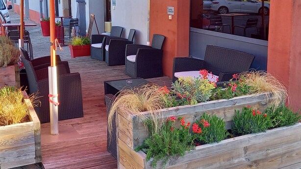 Un espace extérieur aménagé avec des meubles en osier, des parasols rouges et des jardinières en bois ornées de fleurs.