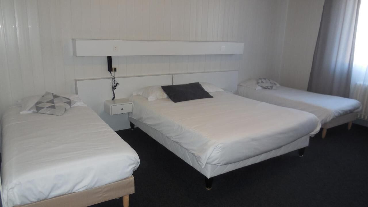 A hotel room with two single beds, a nightstand with a phone, and a headboard with a power outlet.