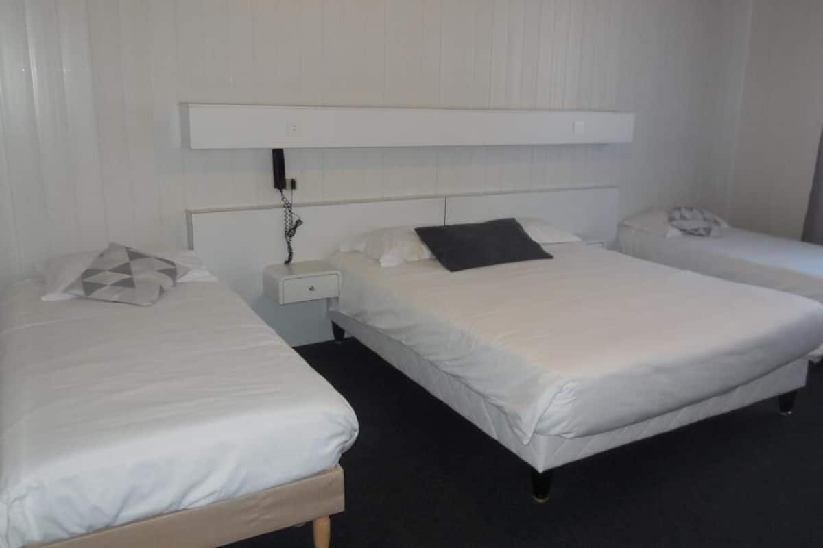 Een hotelkamer met twee enkele bedden, een nachtkastje met een telefoon en een hoofdeinde met een stopcontact.