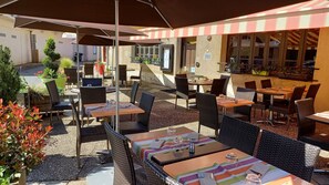 Un patio al aire libre con mobiliario de mimbre, sombrillas y plantas en macetas.