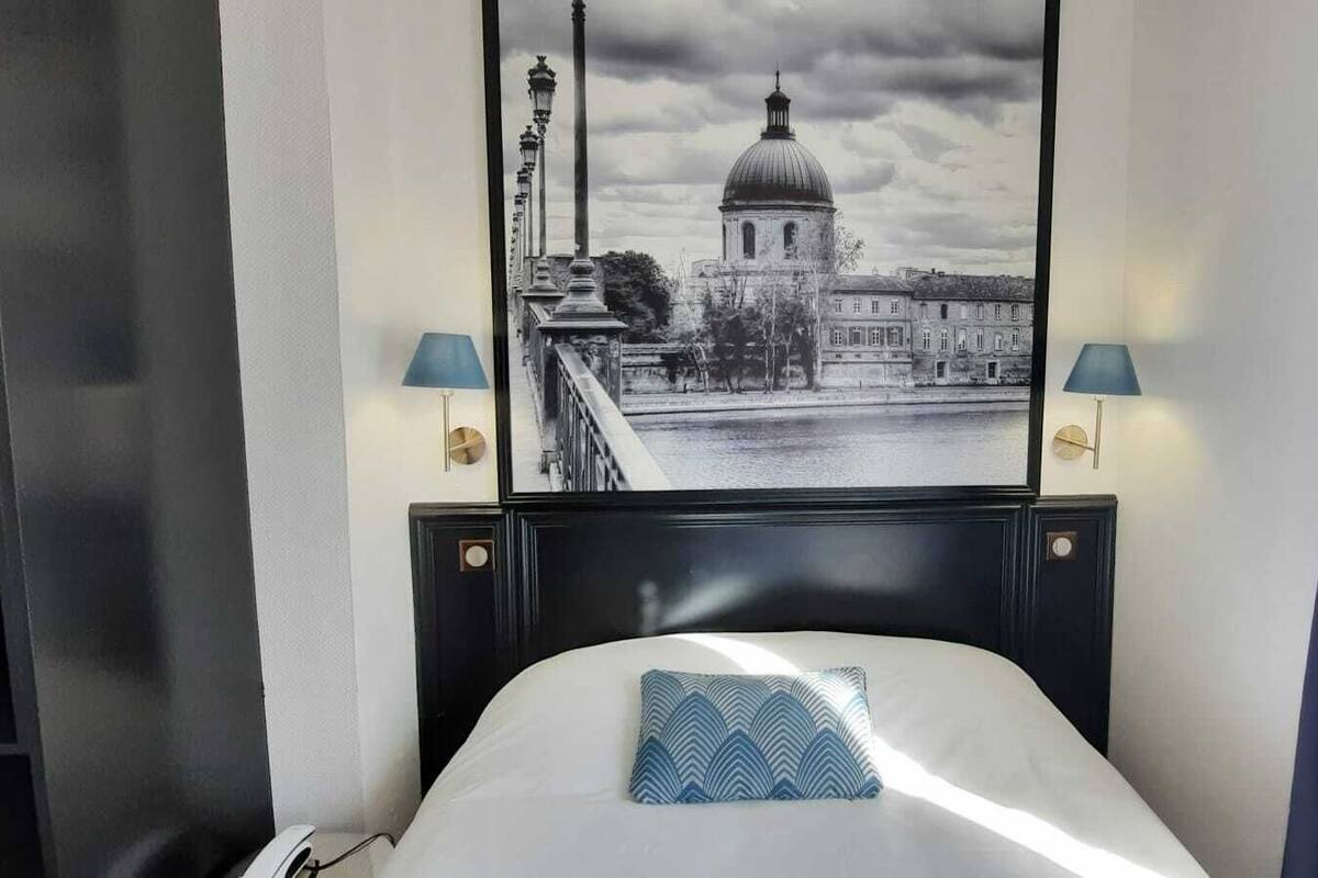 Een hotelkamer met een bed, uitzicht op een stadsbeeld en twee wandlampen.