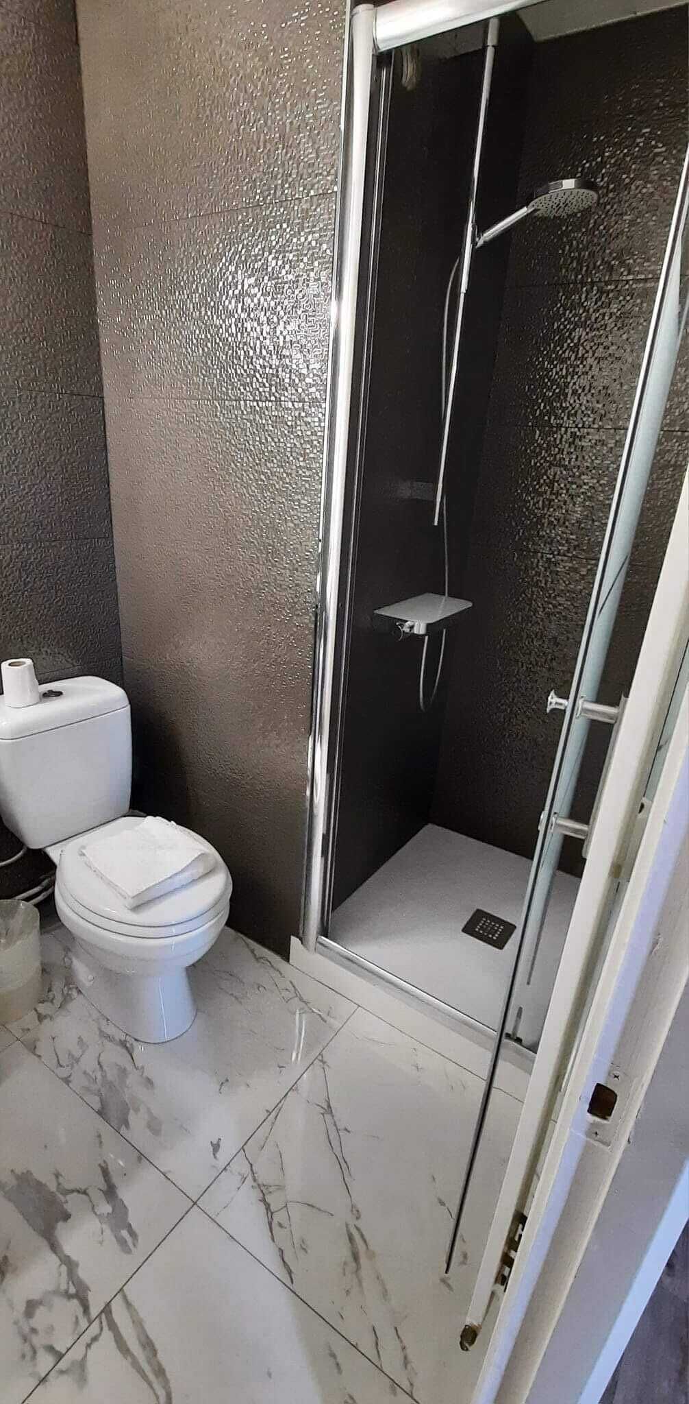 Een badkamer met een toilet, een douche met glazen deur en een marmeren vloer.