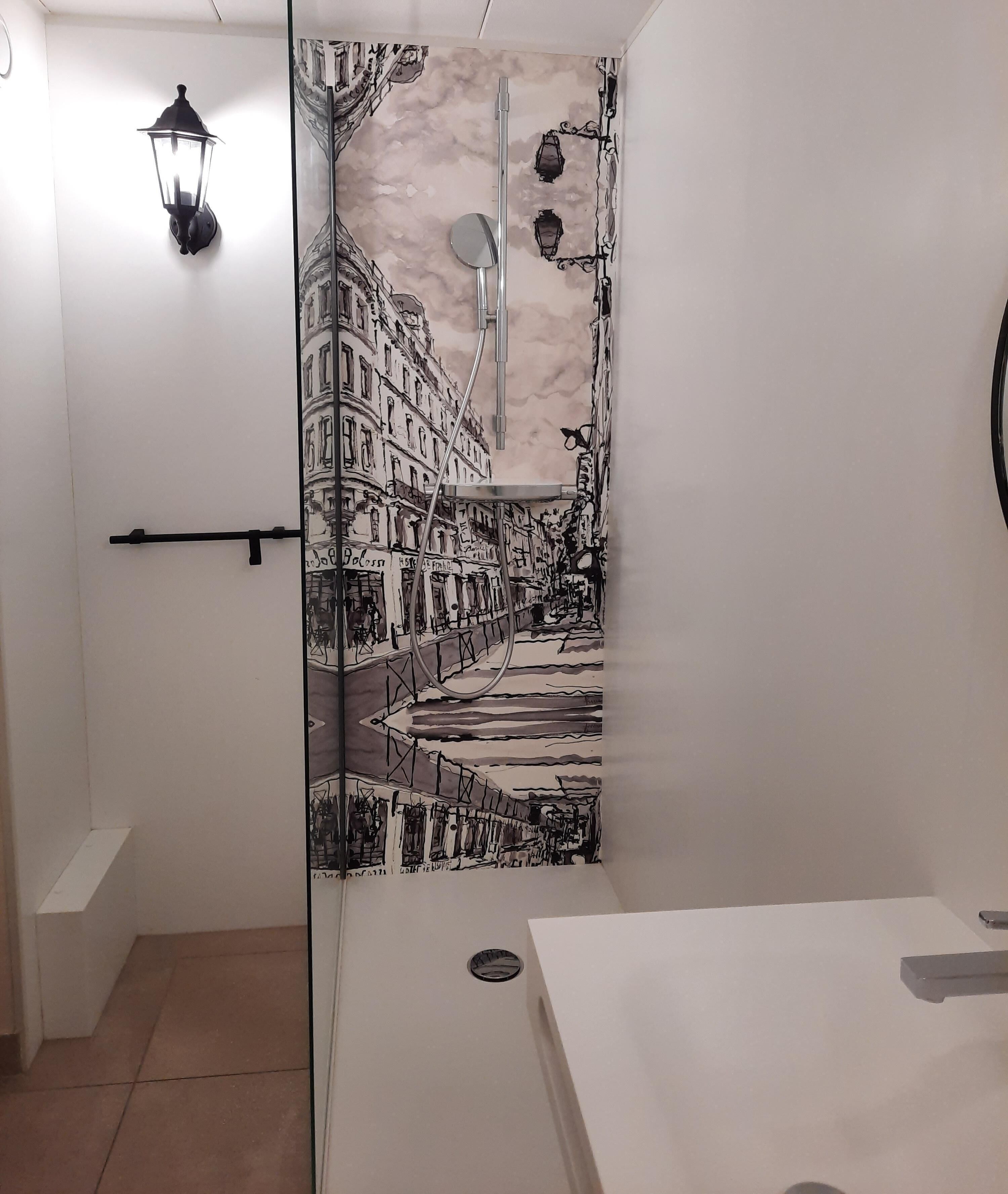 Une salle de bain dotée d’une paroi en verre ornée d’une fresque représentant une scène de rue en noir et blanc, d’un lavabo blanc et d’un porte-serviettes noir.