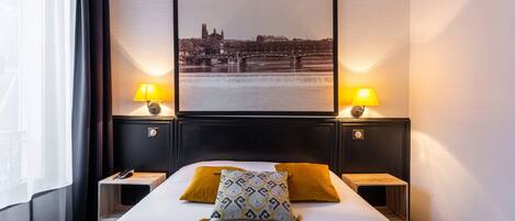 A hotel room with a large bed, two bedside tables, a nightstand, a lamp, and a framed picture of a cityscape.