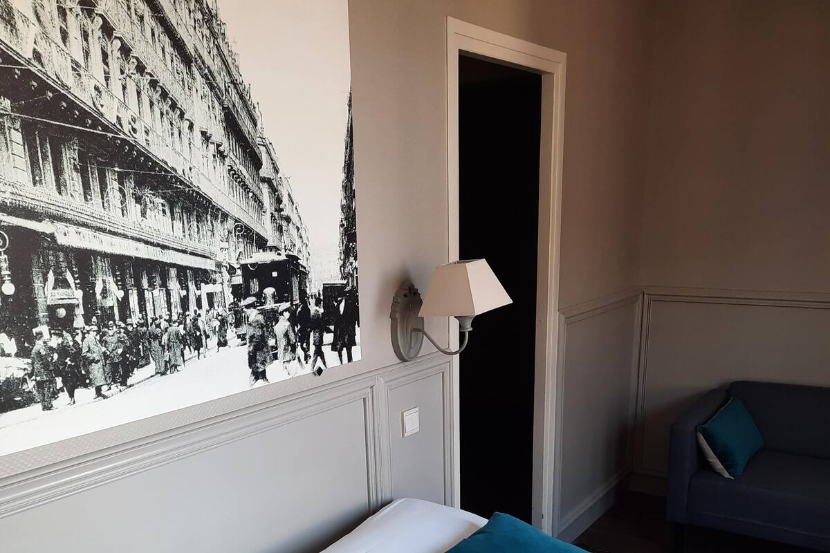 Een hotelkamer met een bed, twee kussens, een nachtkastje, een wandlamp en een deur.