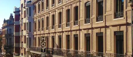 A multi-story hotel with a classic architectural style, featuring balconies with wrought iron railings and a prominent 'HOTEL' sign.
