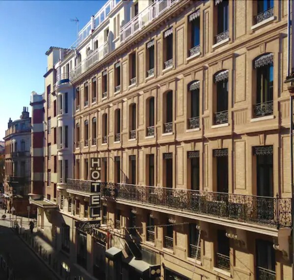 A multi-story hotel with a classic architectural style, featuring balconies with wrought iron railings and a prominent 'HOTEL' sign.