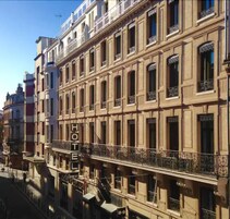 Un hotel de varios pisos con un estilo arquitectónico clásico, con balcones con barandas de hierro forjado y un llamativo letrero que dice 'HOTEL'.