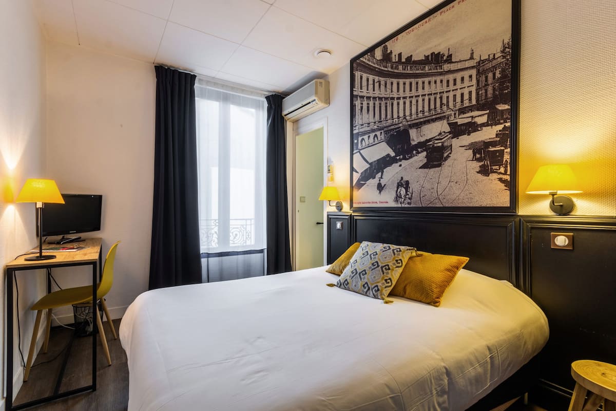 Een hotelkamer met een bed, een bureau met een computer, een stoel en twee lampen.